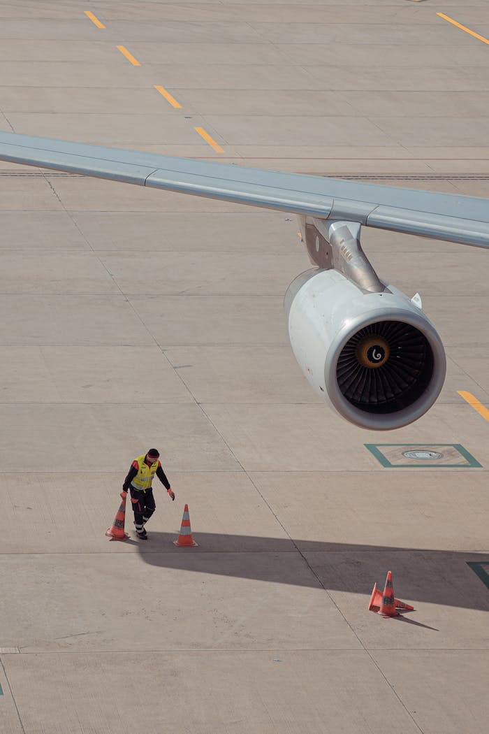 Aviation worker in safety gear checks around a parked airplane at Kloten airport.